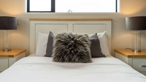 Uma cama com travesseiro fofo, roupa de cama branca e cabeceira de madeira.