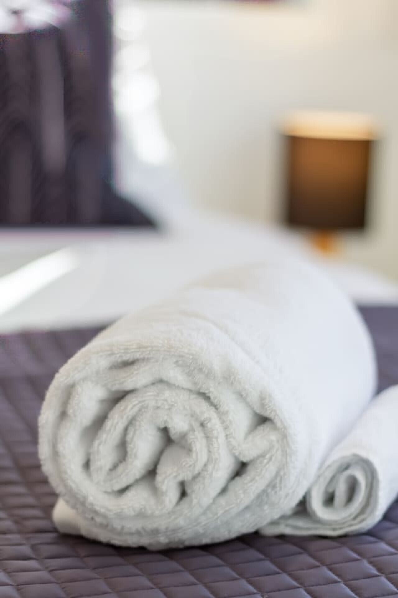 Een opgerolde witte handdoek op een bed met een donkere gewatteerde hoes.