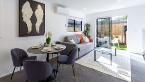 Una sala de estar moderna con un sofá gris, una mesa de centro de cristal y una zona de comedor con una mesa redonda y cuatro sillas.