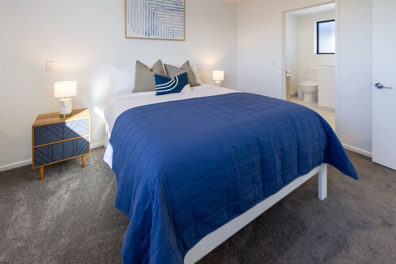 A bedroom with a bed, bedside tables, a nightstand, a door, and a bathroom visible through an open door.