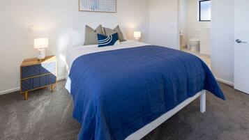 A bedroom with a bed, bedside tables, a nightstand, a door, and a bathroom visible through an open door.