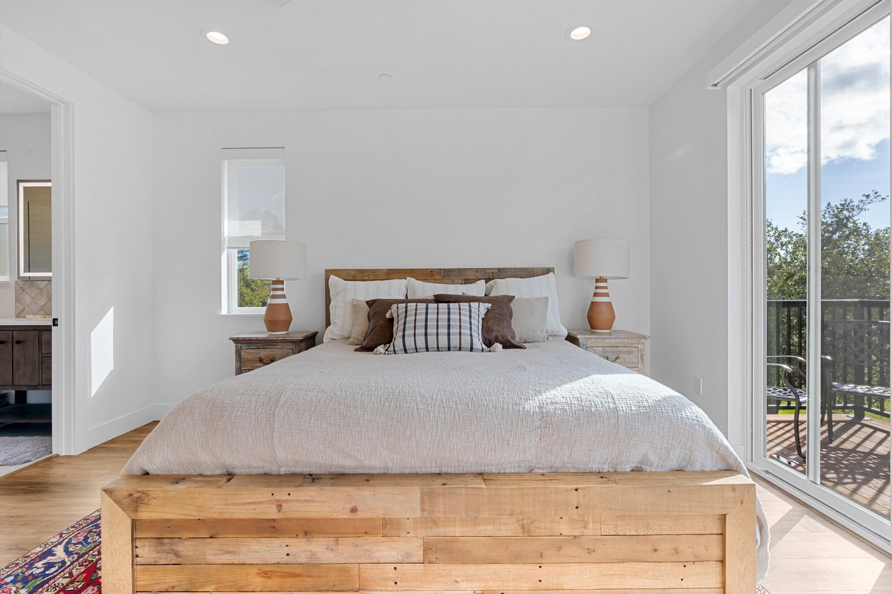 Ein geräumiges Schlafzimmer mit einem großen Bett, einem Holz-Kopfteil und Blick ins Freie durch eine Schiebetür.