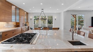 A modern kitchen with a central island, wooden cabinets, and a large window overlooking a deck. - Healdsburg Modern home, 3BR/3.5BA pool, hot tub, outdoor kitchen, WiFi (Healdsburg)
