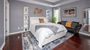 A bedroom with a large bed, a ceiling fan, a gray wall, a white shelf unit, and a painting. - Family-Friendly Birmingham Area Home Near Trussville Sports Complex (Birmingham)