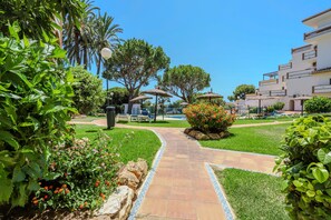 A pathway leading to a seating area with umbrellas, surrounded by greenery and a building with balconies. - Calahonda 2BED apartment - great location (Mijas Costa)