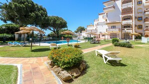 A pool area with lounge chairs and umbrellas, surrounded by a well-maintained lawn and a building with multiple balconies. - Calahonda 2BED apartment - great location (Mijas Costa)