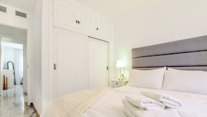 A neatly made bed with white linens and a folded towel, a bedside lamp, and a white wardrobe with a mirror. - Calahonda 2BED apartment - great location (Mijas Costa)