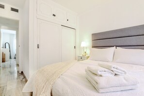 A neatly made bed with white linens and a folded towel, a bedside lamp, and a white wardrobe with a mirror. - Calahonda 2BED apartment - great location (Mijas Costa)
