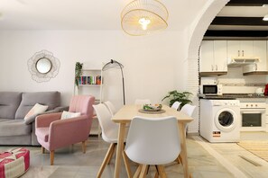 Ein modernes Wohnzimmer mit Sofa, Sessel, Esstisch und einer Waschmaschine im Hintergrund.