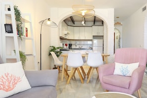 A modern living room with a dining area, white brick walls, and a kitchen in the background. - Calahonda 2-Bedroom Apartment - Great Location (Mijas Costa)
