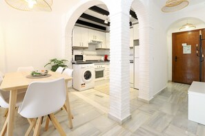 A modern kitchen with white cabinetry, a washing machine, and a dining area with a table and chairs.