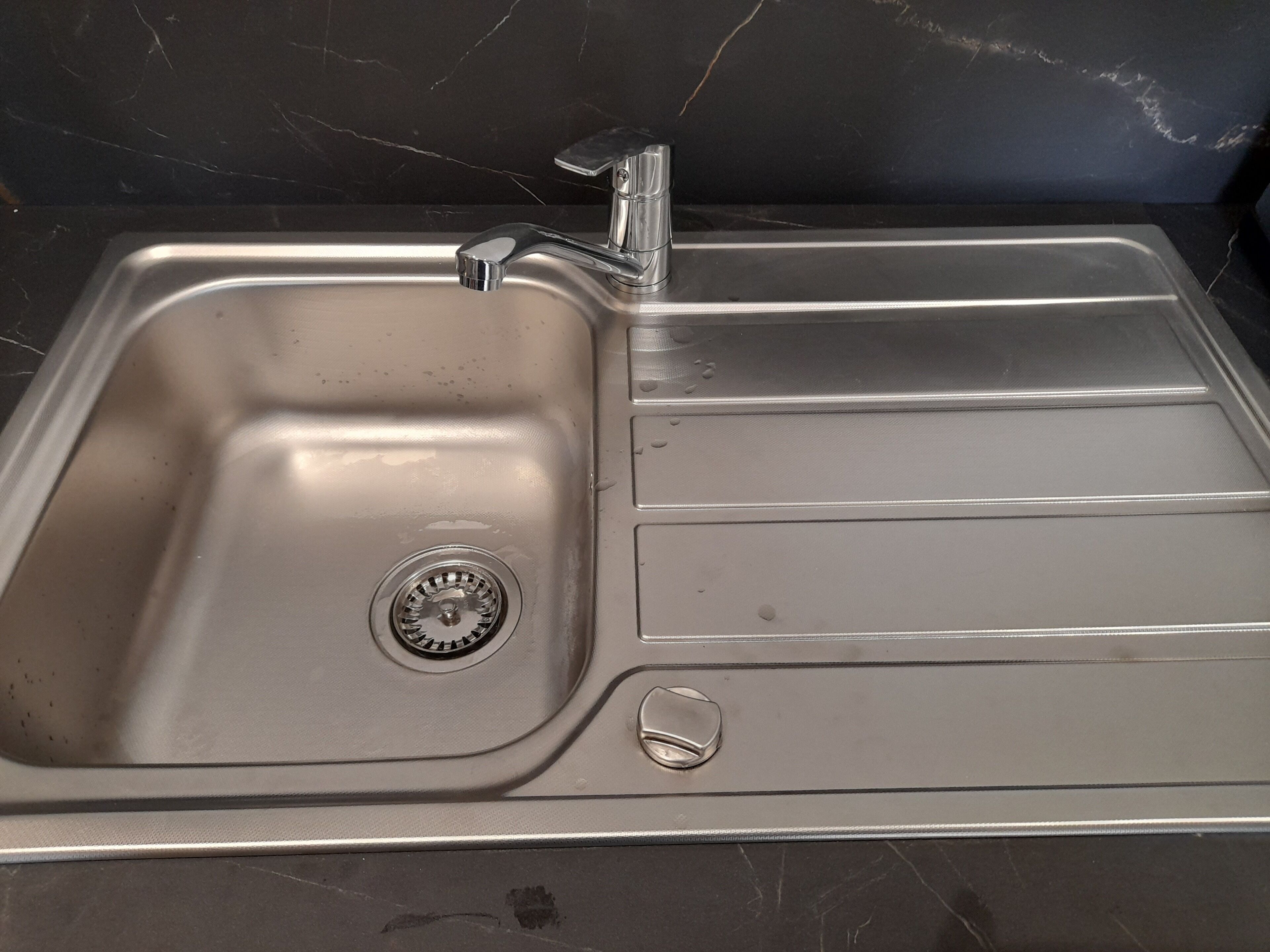 A stainless steel kitchen sink with a single faucet, a drain, and a soap dish.
