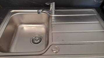 A stainless steel kitchen sink with a single faucet, a drain, and a soap dish.