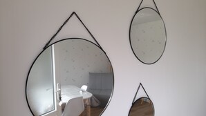 Drie wandspiegels met zwarte frames en kettingen, die een kamer met een witte tafel en stoelen weerspiegelen.