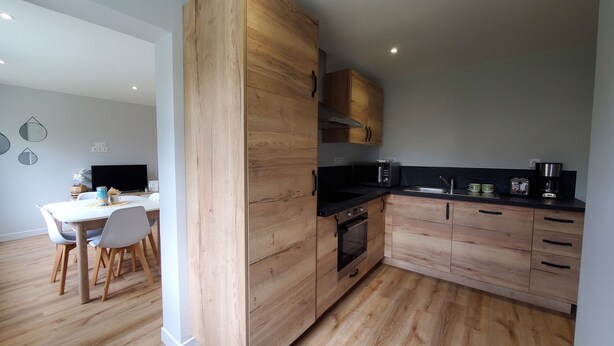 Een moderne keuken met houten kastjes, een zwart aanrecht en een eethoek met een witte tafel en stoelen.