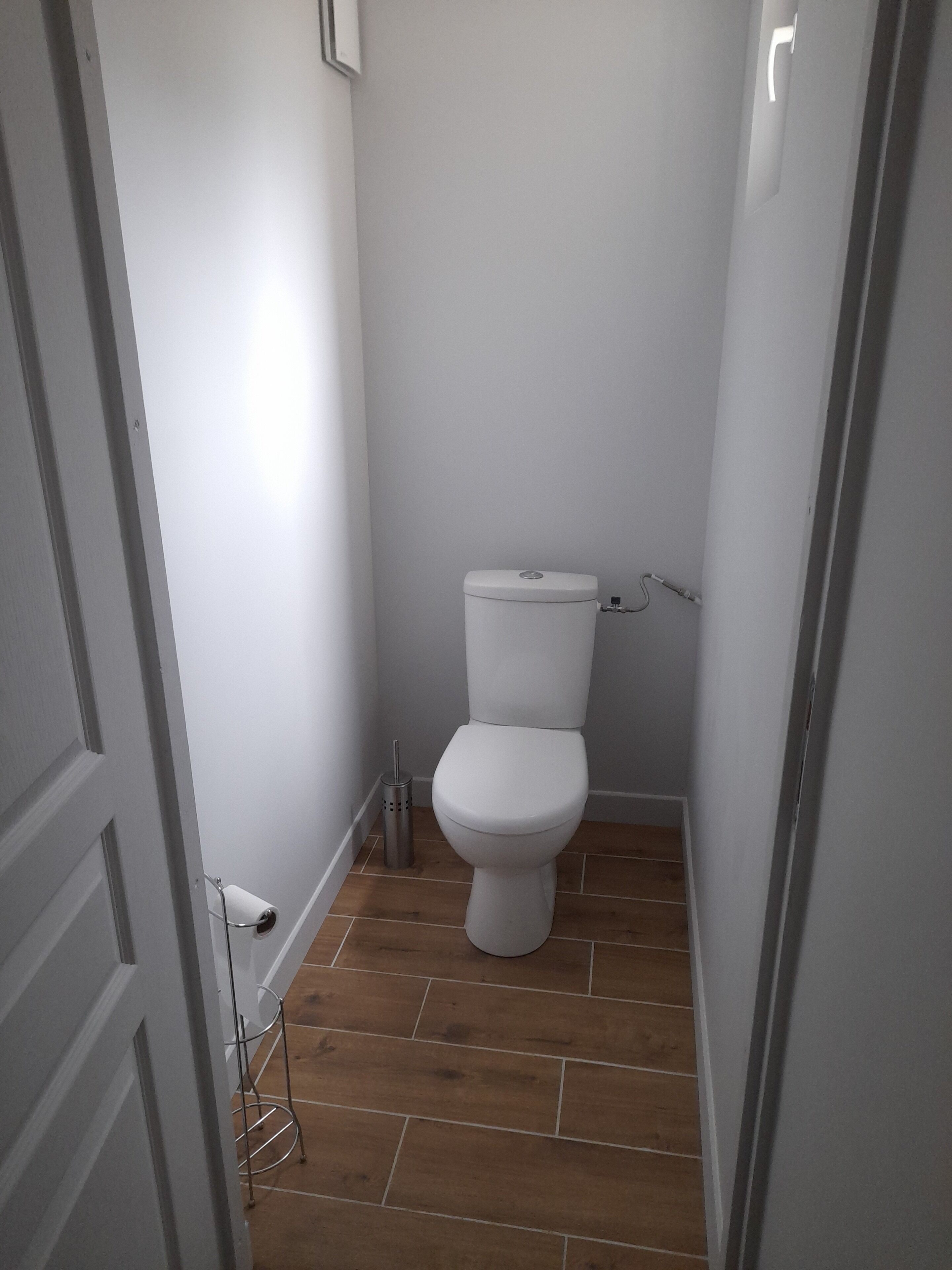 Ein kleines, schmales Badezimmer mit Toilette, einem Metall-Mülleimer und einer weißen Tür.