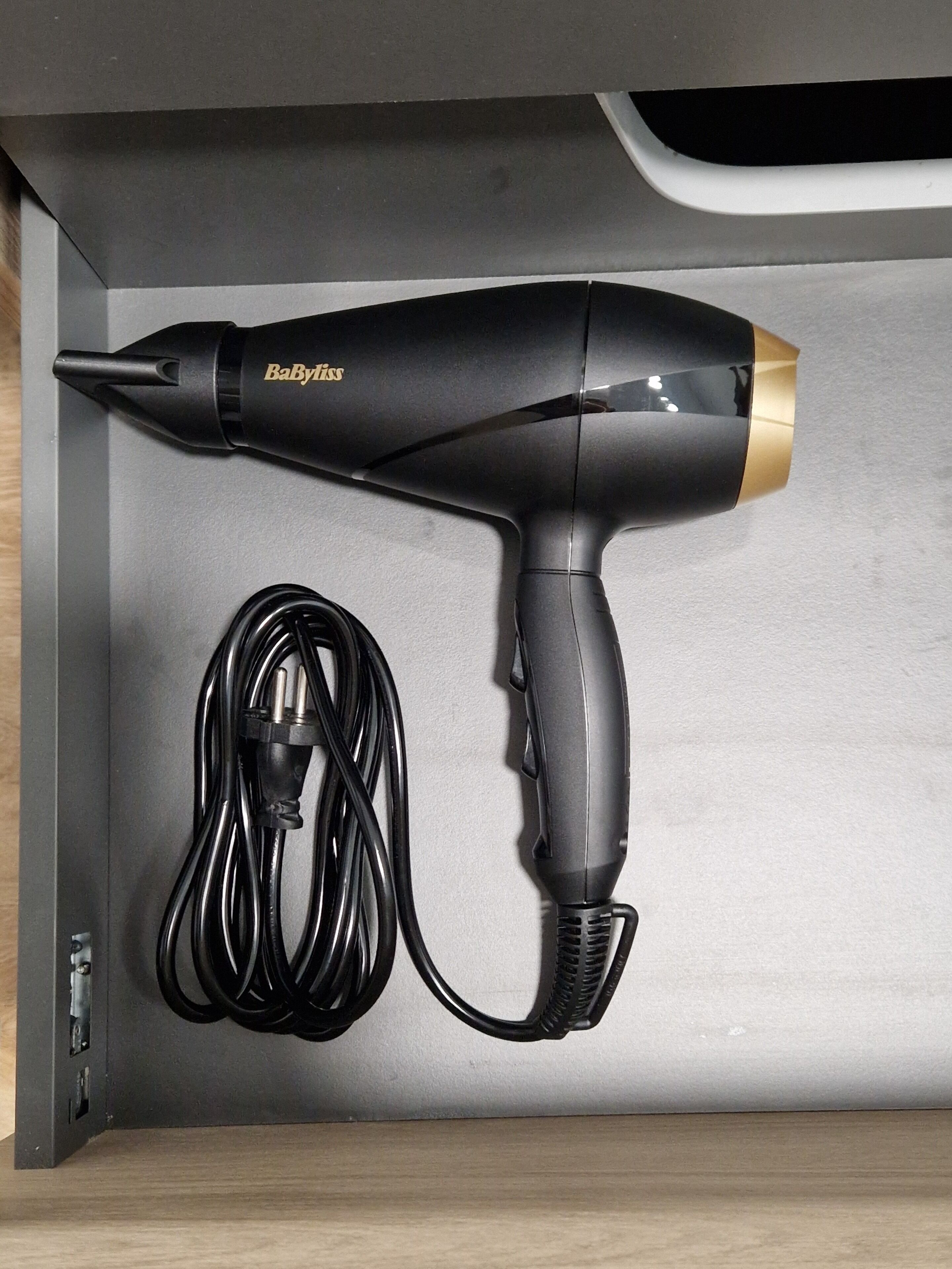 A black and gold hair dryer with a cord, placed in a drawer.