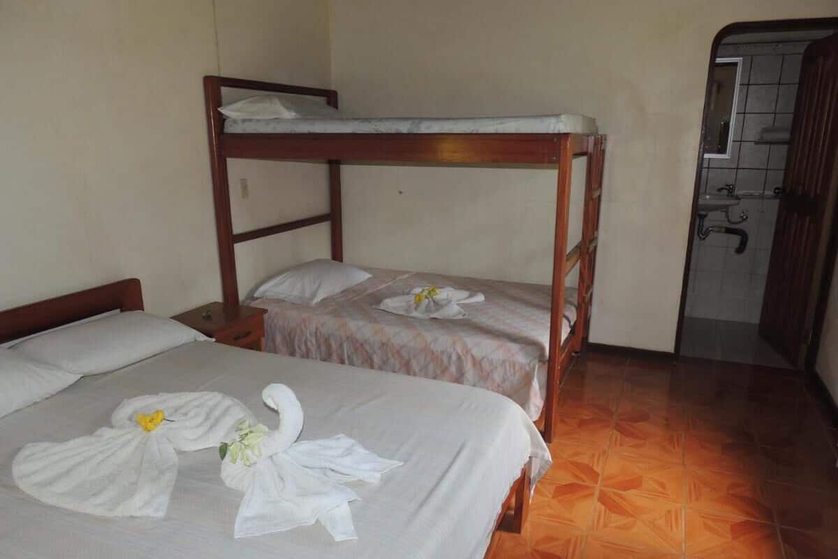 Une chambre avec deux lits, dont un lit superposé, et une petite salle de bain avec un lavabo et un miroir.