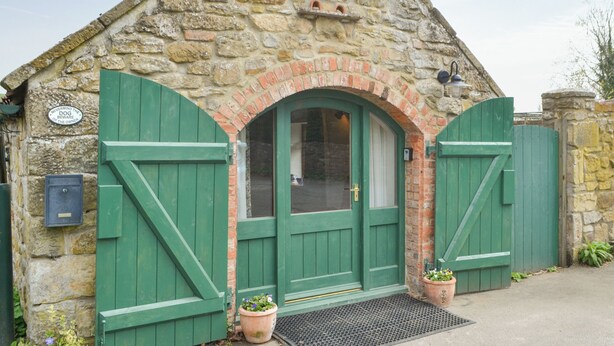 A stone building with green shutters and a door, featuring a sign that reads "NEVERMIND THE DOG BEWARE OF THE OWNER". - 1 bedroom accommodation in Newton-on-the-Moor (Newton-on-the-Moor)