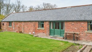 A brick building with a sloped roof, a green door, and a small garden area with a bench and two spherical lights. - 1 bedroom accommodation in Newton-on-the-Moor (Newton-on-the-Moor)