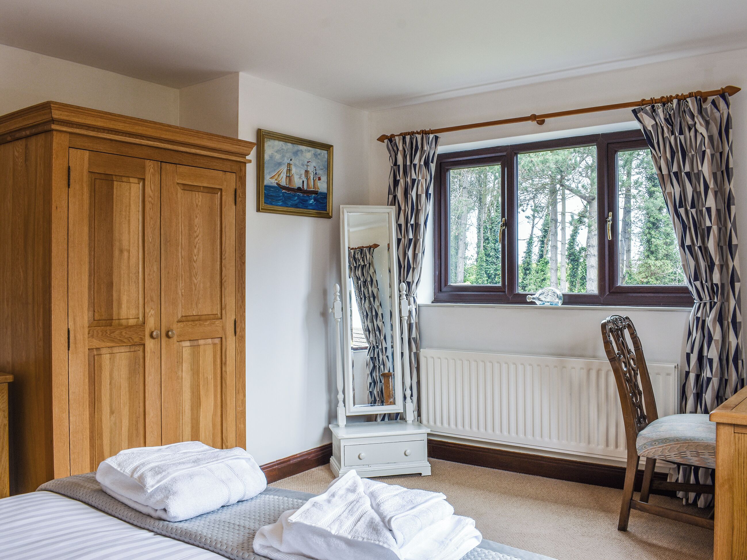 Ein Schlafzimmer mit einem Bett, einem Holzschrank, einem Stuhl, einem Fenster mit Vorhängen und einer Heizung.