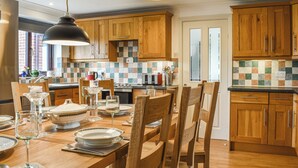 A modern kitchen with wooden cabinets, a tiled backsplash, and a dining area set for a meal. - 5 bedroom accommodation in Runswick Bay, near Whitby (Runswick Bay, near Whitby)