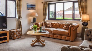 A living room with a leather sofa, a wooden coffee table, and a television on a stand. - 5 bedroom accommodation in Runswick Bay, near Whitby (Runswick Bay, near Whitby)