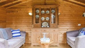 A cozy cabin interior with wooden walls, a ceiling fan, a cabinet with dishes, and two sofas. - 5 bedroom accommodation in Runswick Bay, near Whitby (Runswick Bay, near Whitby)