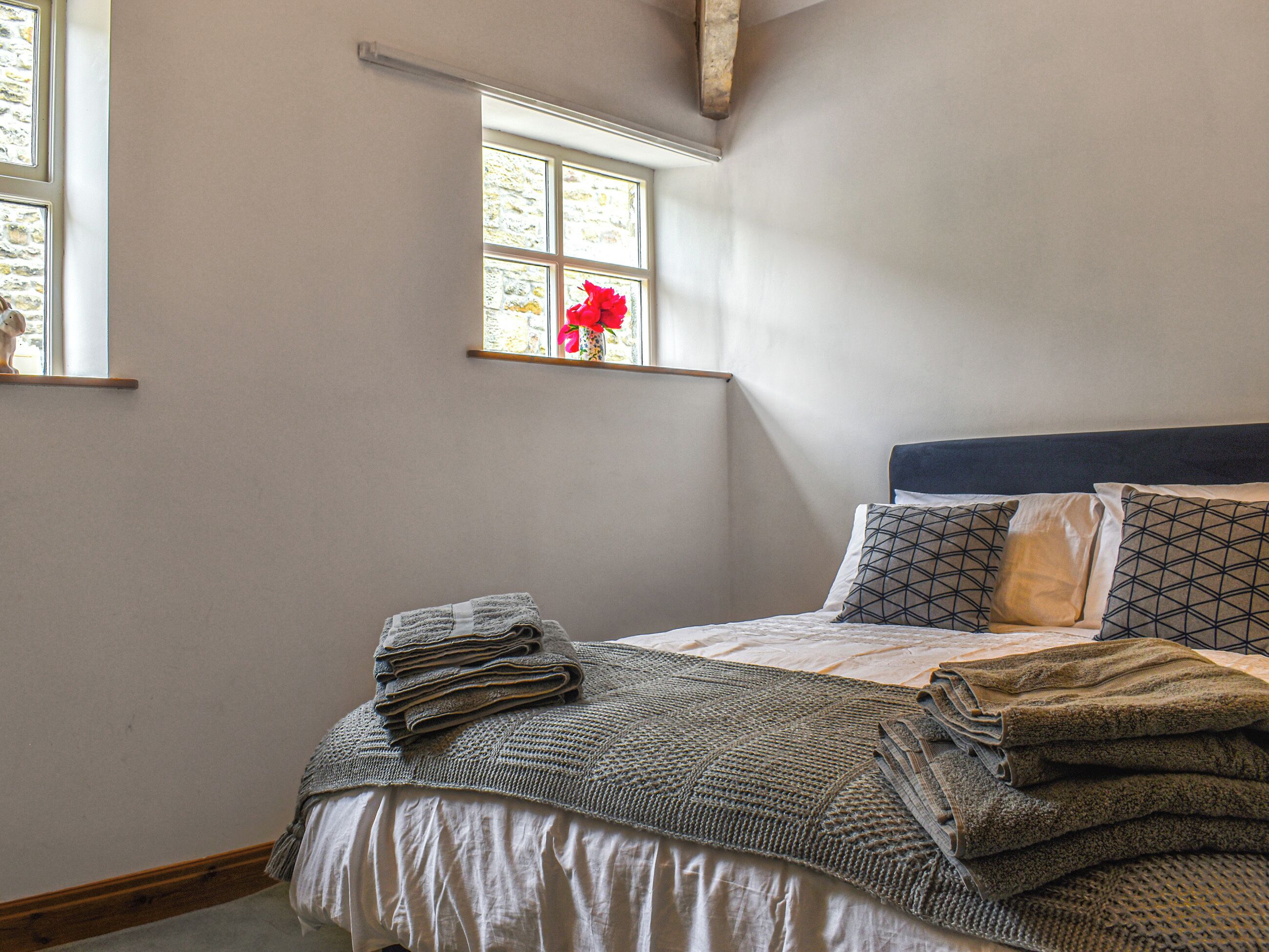 Une chambre à coucher avec un lit, des oreillers, une fenêtre ornée d’une fleur et une vue sur l’extérieur.