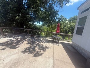 A patio with a table and chairs, a red umbrella, and a white building in the background. - Tiny House on Center Hill Lake (Baxter)