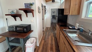 Una cocina compacta con armarios de madera, un microondas, un lavabo y un pequeño cubo de basura.