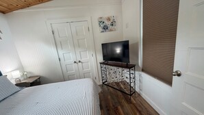 Un dormitorio con cama, televisor sobre un mueble, una puerta y una ventana con persianas.