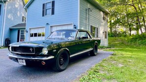 Ein schwarzes Oldtimer-Auto vor einem blauen Haus mit Garage.