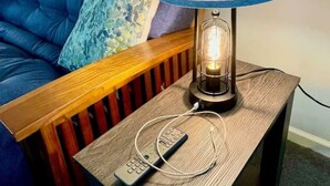 Ein Zimmer mit einem blauen Sofa, einem Holznachttisch und einer Lampe mit blauem Lampenschirm.