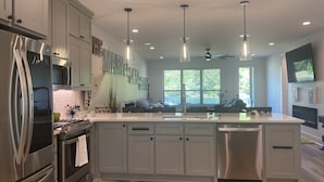 A modern kitchen with stainless steel appliances, a large island, pendant lighting, and a view of the outdoors. - Marvel Lake House Too (Hot Springs)