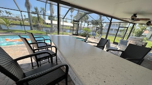 Un espace bar extérieur abrité, avec vue sur la piscine, des fauteuils en osier et un barbecue.