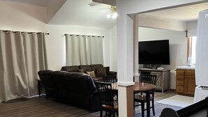 Ein modernes Wohnzimmer mit einer Couch, einem Esstisch und Stühlen. An der Wand ist ein Flachbildfernseher angebracht.