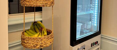 A refrigerator with a lighted interior, a wicker basket with bananas and bread, and a window with a view of the outside.