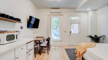 A compact, well-lit room with a bed, a dining table with chairs, a microwave, a television, and a door leading outside.