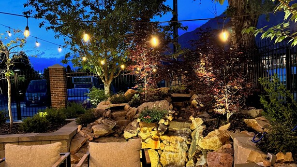 An outdoor patio area with seating, a small waterfall, and string lights. - Art City Inn (Springville)