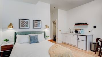 Un dormitorio moderno con cama, mesitas de noche y una pequeña kitchenette.