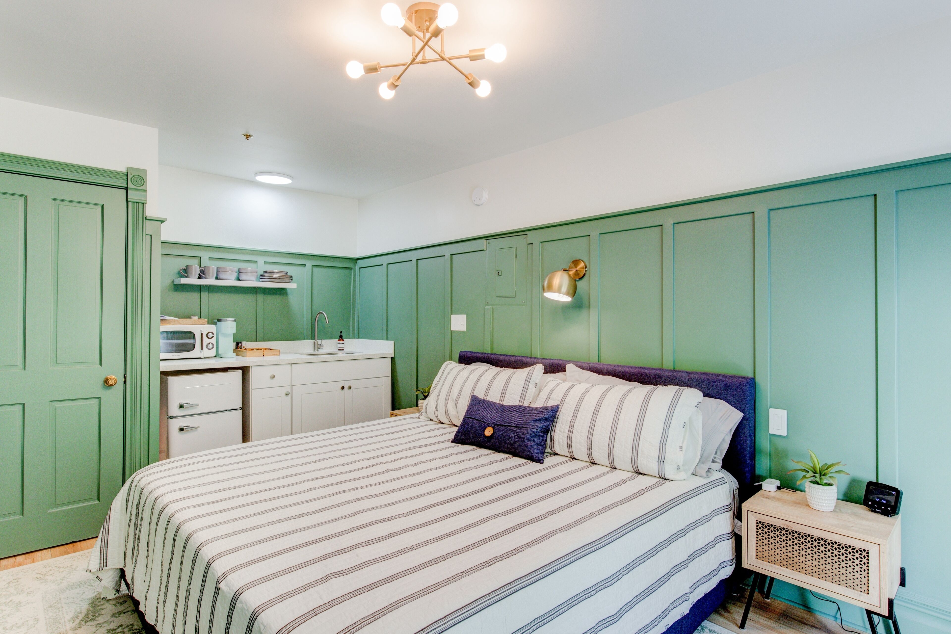 A bedroom with a bed, bedside table, and a small kitchenette.