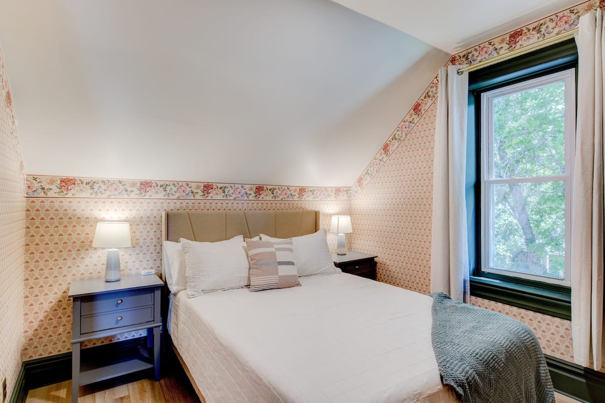 Una camera da letto con un letto, due comodini con lampade, una finestra con tende e carta da parati floreale.