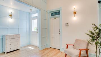 Una habitación con piso de madera, un aparador blanco, un sillón beige y una puerta con detalles azules.