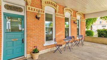 A brick building with a teal door labeled "Lobby" and a sign for "Kearns Hotel." There are outdoor chairs and a potted plant near the entrance.