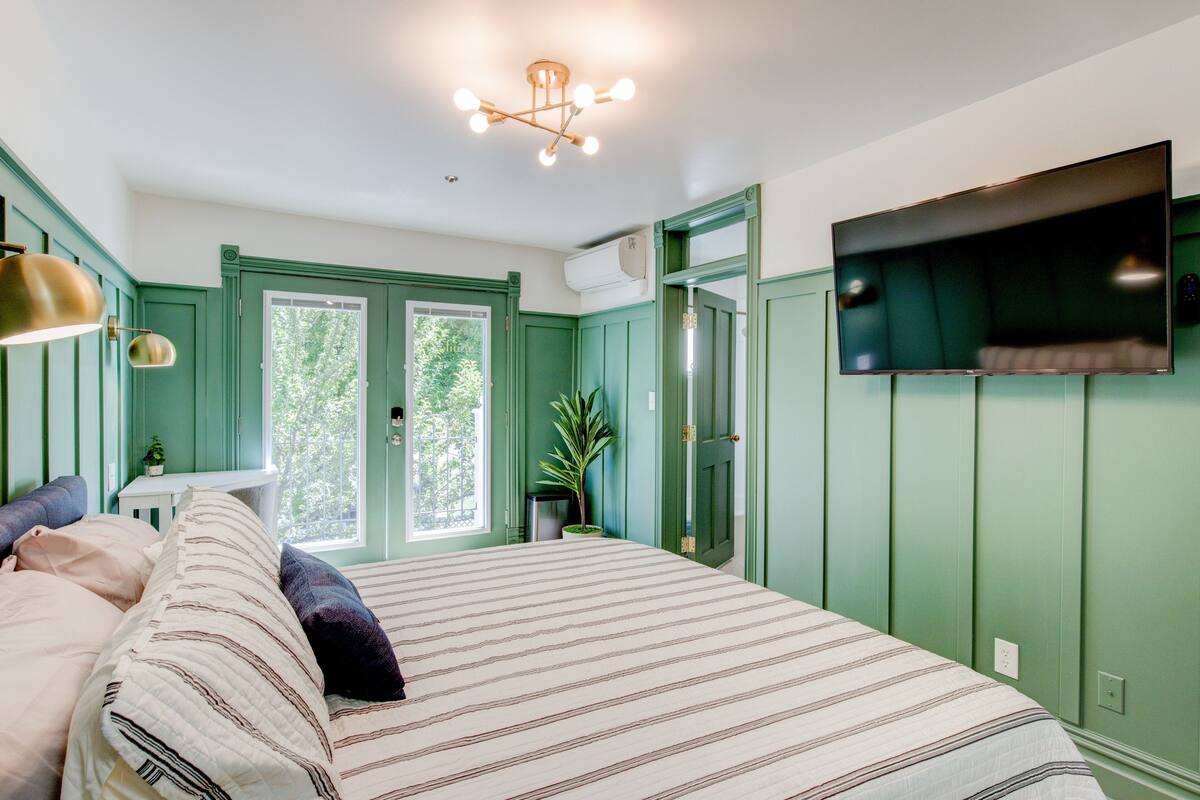 Una camera da letto con un letto, una TV a muro e una finestra vista alberi.