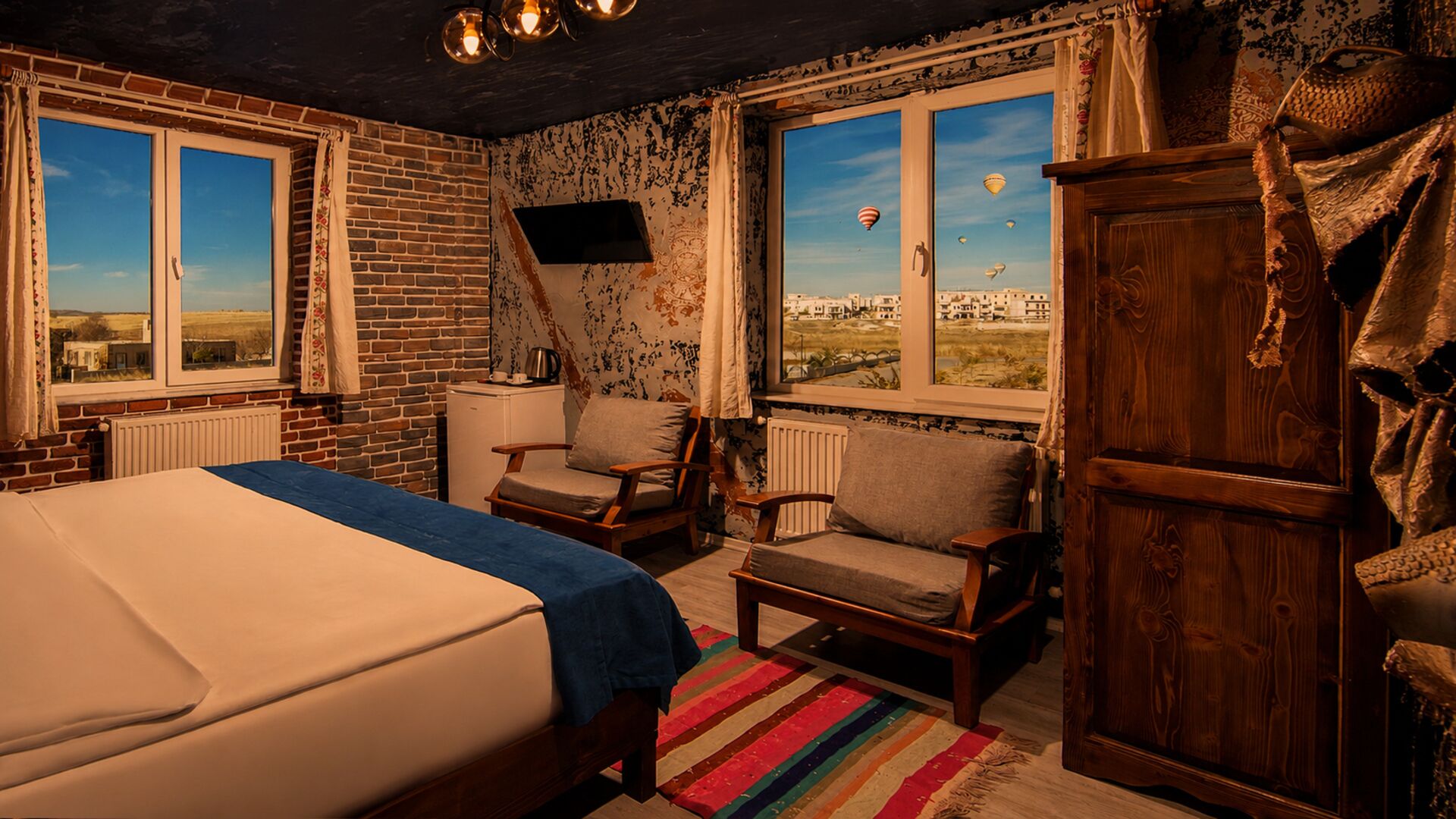 A bedroom with a bed, two chairs, a radiator, a window with a view of hot air balloons, and a wooden wardrobe.