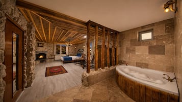 Un baño con paredes de piedra, una bañera independiente, suelo de madera y chimenea de piedra.