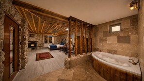 Ein Badezimmer mit Steinwänden, einer freistehenden Badewanne, Holzboden und einem Steinkamin.