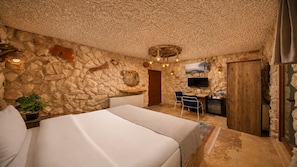 A stone-walled bedroom with a bed, a desk, and a television. - Moonlight  Of Cappadocia (Nevsehir)